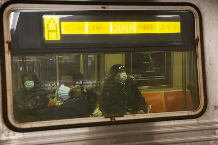 Masked subway riders seen on an A from from outside the train car, through the window